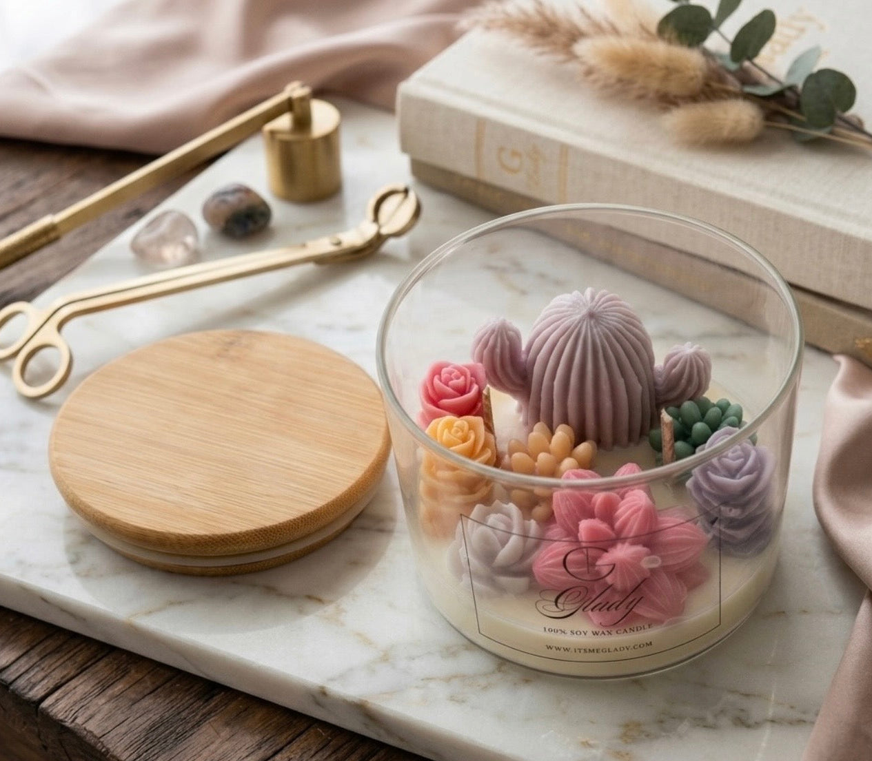 Decorative candle with cactus design in a glass jar on a marble surface.